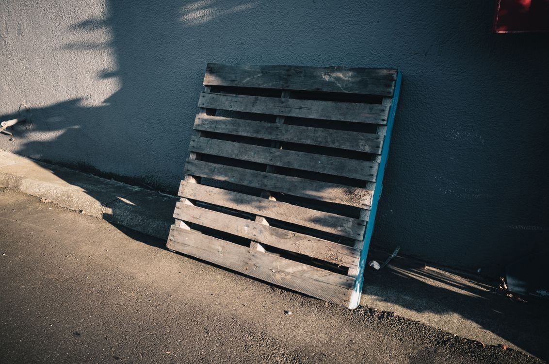 Single wooden pallet leaning against a wall, showing deck boards and stringers of a standard pallet